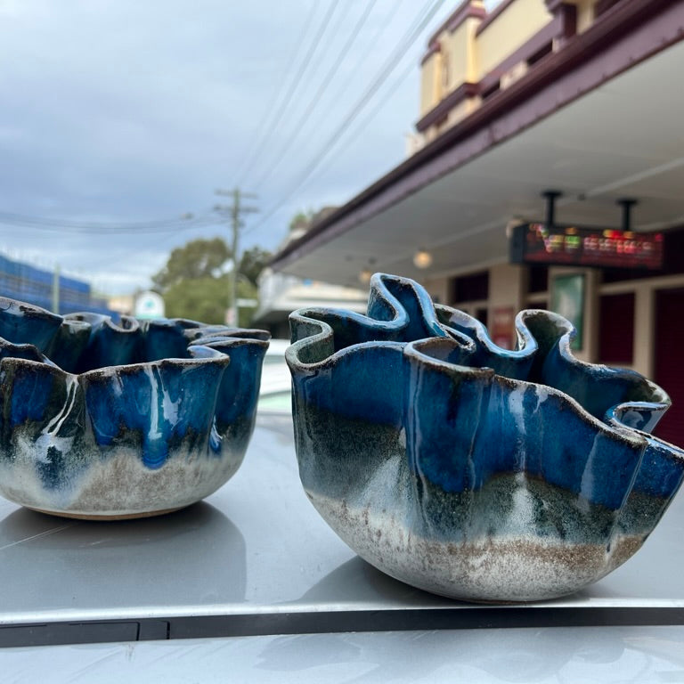 Two blue ceramic bowls on a car hood with a building and power lines in the background.